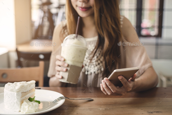 Young woman using smart phone and eating cake in cafe