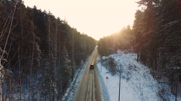 Car Rides By Road in Snow-covered Forest. Footage. Rays of the Morning Sun. Aerial View. Aerial View alt