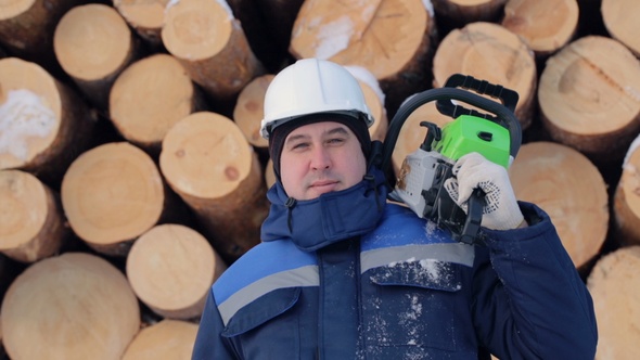 Worker With Chain Saw Against Pile of Logs