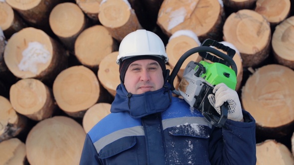 Worker With Chain Saw Against Pile of Logs