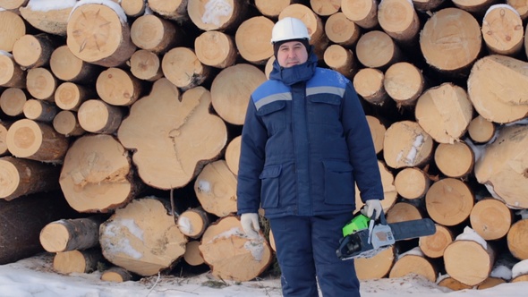 Worker With Chain Saw Against Pile of Logs