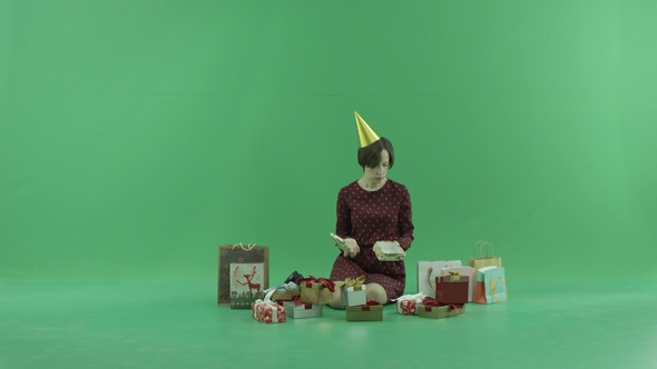 A Young Woman Is Sitting and Opening Empty Gift Boxes Around Her on the Green Screen
