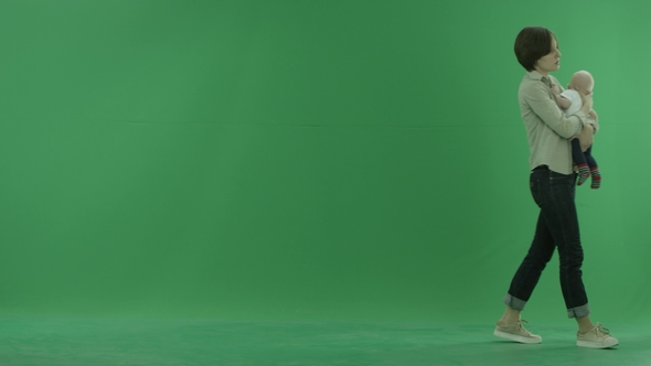 A Young Woman Going From the Left Side with Her Baby on the Green Screen