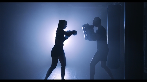 Young Woman Training with a Coach in a Boxing Club in a Smoky Gym alt