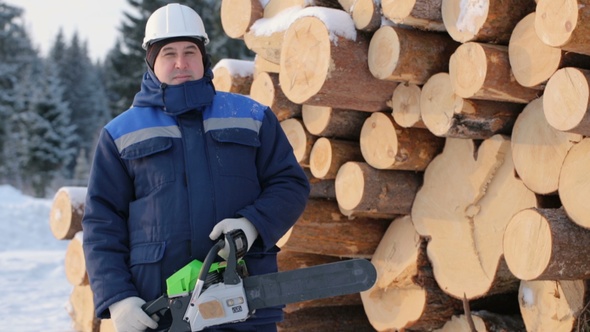 Worker With Chain Saw Against Pile of Logs