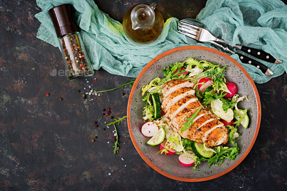 Bowl with salad of fresh vegetables and baked chicken breast on a dark background. - Stock Photo - Images