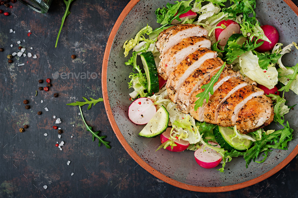 Bowl with salad of fresh vegetables and baked chicken breast on a dark background. - Stock Photo - Images