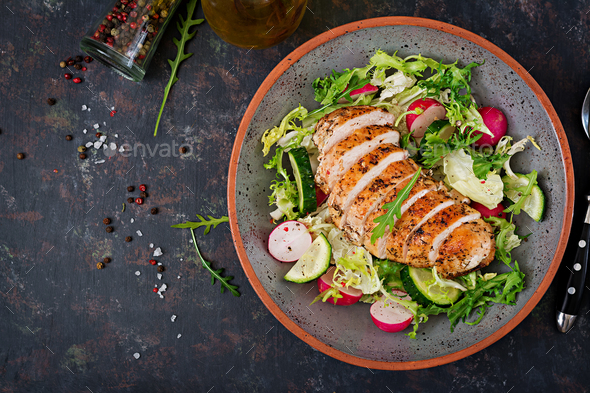Bowl with salad of fresh vegetables and baked chicken breast on a dark background. - Stock Photo - Images