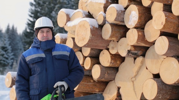 Worker With Chain Saw Against Pile of Logs