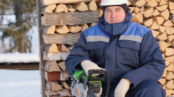 Worker With Chain Saw Against Pile of Logs