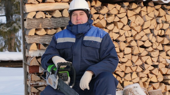 Worker With Chain Saw Against Pile of Logs