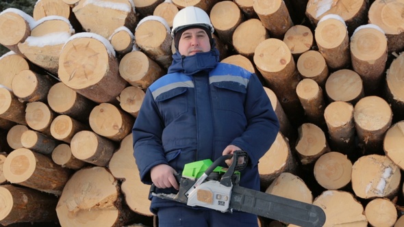 Worker With Chain Saw Against Pile of Logs