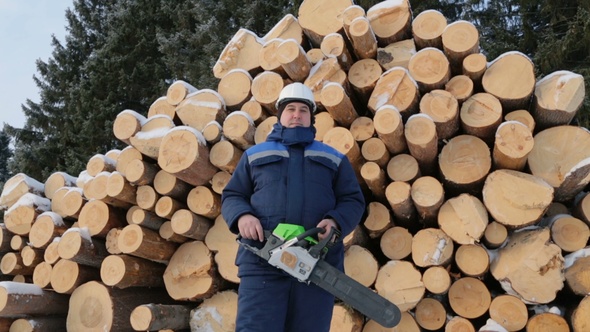 Worker With Chain Saw Against Pile of Logs