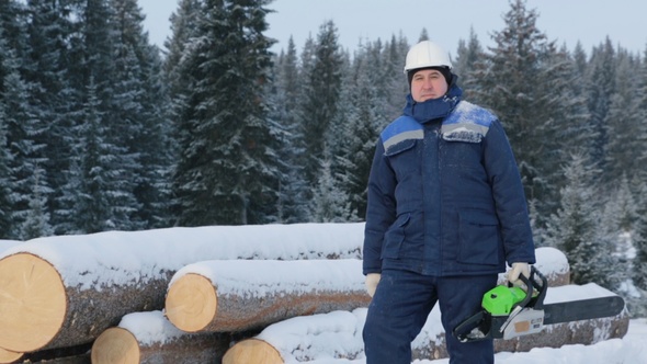 Worker With Chain Saw Near Pile of Logs in the Forest