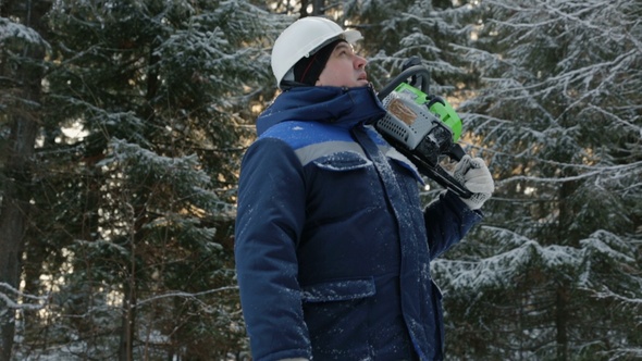 Worker With Chain Saw on Shoulder Going Through Winter Forest