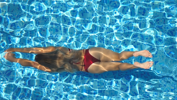 Unrecognizable Young Woman Swimming Under the Water in Pool and Emerging on the Surface alt