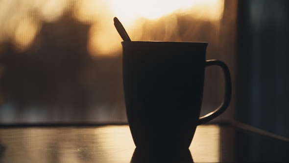Cup of Hot Coffee or Tea at Window Side Abstract Blur Background. Evening Sunset