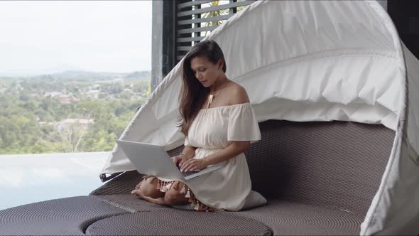 Adult Barefooted Woman Using Laptop on Balcony Against Landscape at Tropical Resort alt