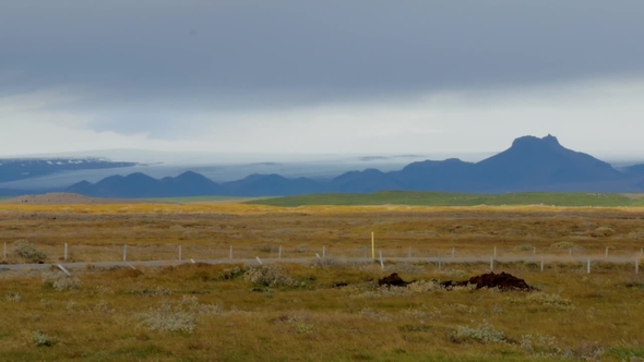 Yellowed Fields Near Dark Hills in Iceland and Low Rainy Clouds in Autumn Day