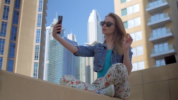 Young Pretty Girl Is Taking Selfie By Smartphone Playing with Her Hair, Sitting Crossing Legs