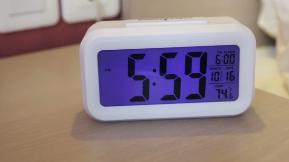 Electronic Alarm Clock Stands on a Bedside Table in the Room