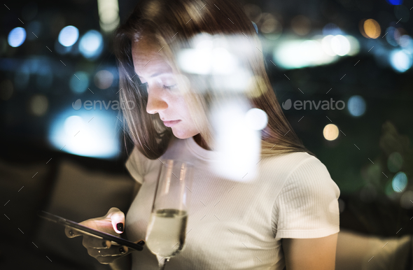 Serious young woman using a smartphone at a rooftop bar in the e - Stock Photo - Images