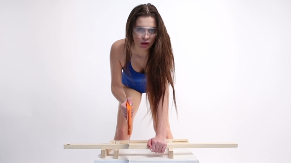 a Sexy Woman in a Blue Swimsuit Sawing Wooden Beams with Saw. the Beautiful Girl Moves Erotically.