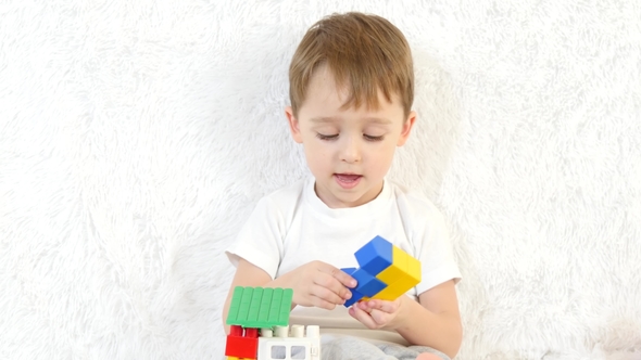 The Little Boy Builds a Toy House of Colored Blocks, Sitting on a White ...