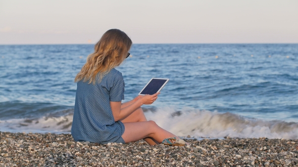 Blonde Woman Reading E-book By Tablet, on Beach in Evening Time