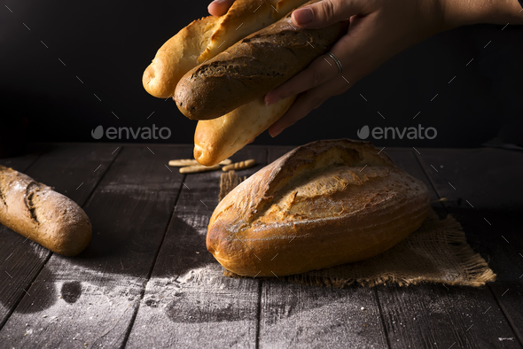 Close-up of woman hands take fresh bread. Dark photo - Stock Photo - Images