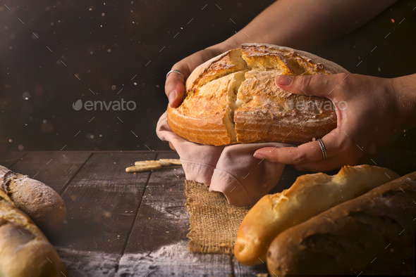 Loaf of fresh baked wheat bread in woman's hands in sunshine. Rustic day light in dark room. - Stock Photo - Images