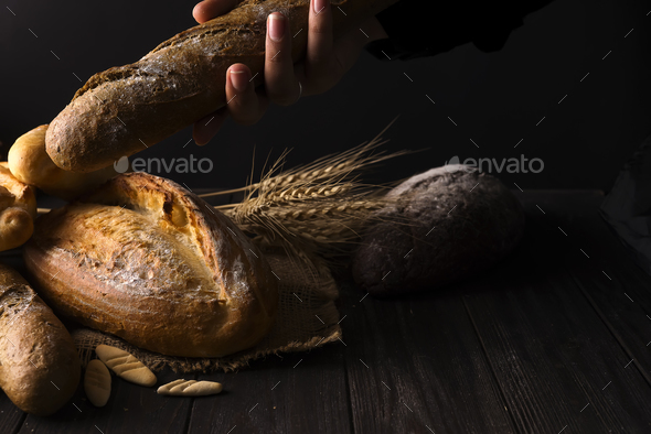 Close-up of woman hands take fresh bread. Dark photo - Stock Photo - Images