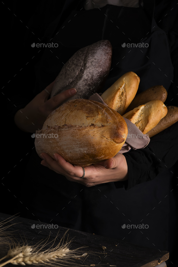 Woman holding tasty fresh bread sorts on a dark - Stock Photo - Images