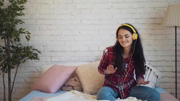 the Girl Listens To Music with Headphones and Sitting on the Bed Dancing