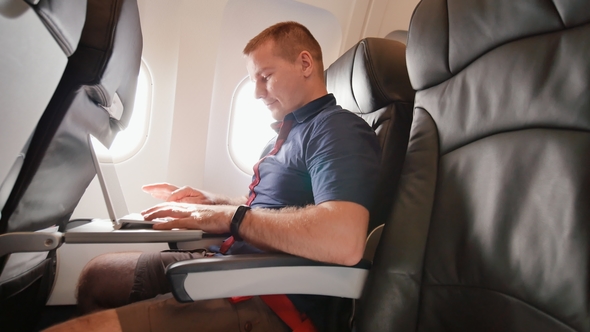 A Young Man Was Sitting on the Plane and Working on His Laptop Before Departure. alt