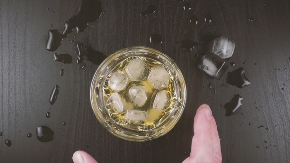 Man's Hand Takes a Glass of Whiskey From the Table