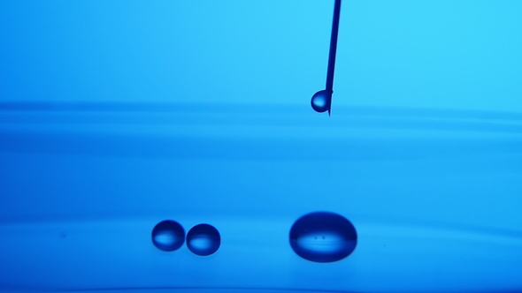 Crystaline Water Drops Fall From a Metallic Needle on Blue Surface in a Lab