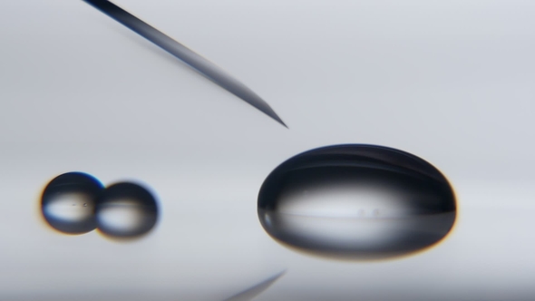 Sparkling Water Drop Is Absorbed From a Metallic Needle on Grey Surface in a Lab