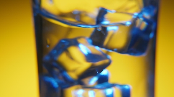 Five Ice Cubes Are Shaken in a Crystal-clear Glass in the Yellow Background
