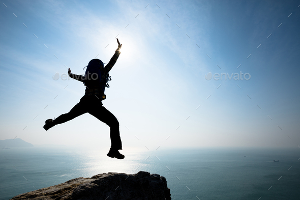 Hipster backpacker jumping on sunrise seaside cliff edge - Stock Photo - Images