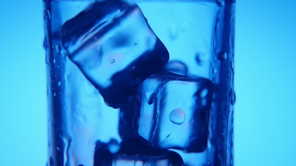 Bluish Ice Cubes in a Glass and Water Pouring in It with Shining Bubbles