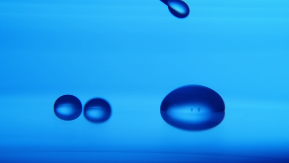 Sparkling Water Drops Fall From a Metallic Needle on Blue Surface in a Lab