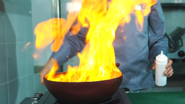 Chef Cooking With Fire In Frying Pan. Professional Chef in a Commercial Kitchen Cooking