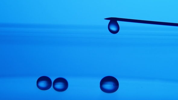 Shining Water Drops Come Down From a Metallic Needle on Blue Surface in a Lab