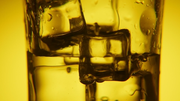 Golden Ice Cubes in a Glass and Water Pouring in It with Shining Bubbles