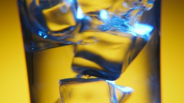 Several Ice Cubes Are Dancing in a Clear Glass in the Yellow Background