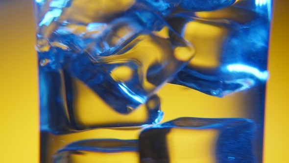 Five Ice Cubes Are Dancing in a Transparent Glass in the Yellow Background
