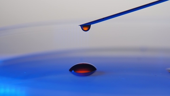 Drops of Red Liquid Fall From a Needle on Blue Surface in the Grey Background