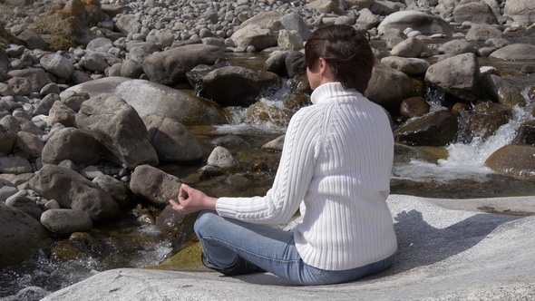 Woman Meditating Next To a Mountain Stream