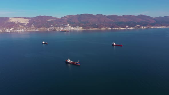 Aerial View, Vessels Drift on Calm Blue Ocean Surface Against Hilly Coast alt